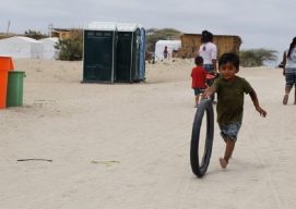 A boy runs behind a tire on a dirt esplanade